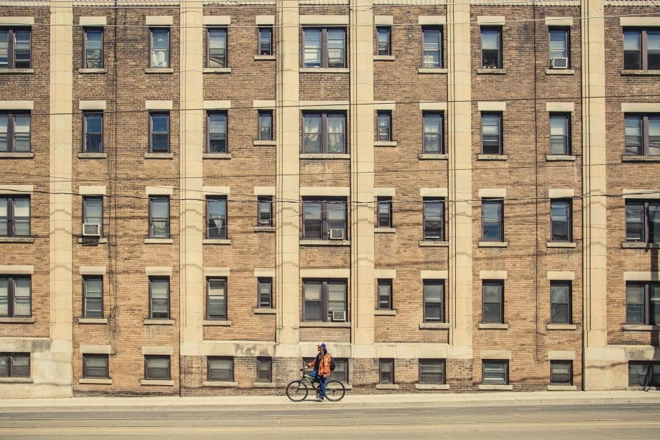 A brick walk-up apartment building with a cyclist passing in front
