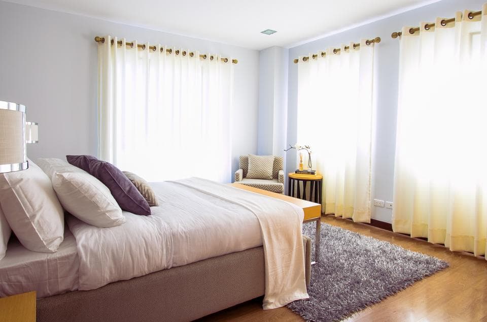 A bedroom with a made bed, armchair and sheer curtains