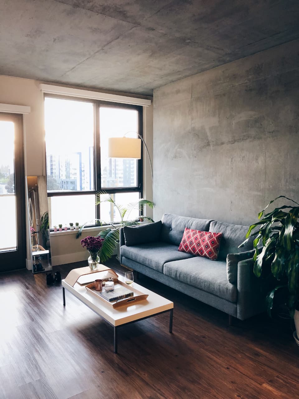 A studio apartment with a grey sofa below tall windows